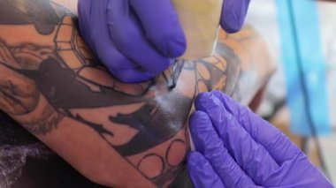 Tattoo artist make a black tattoo on mans skin with a tattoo machine. Close up