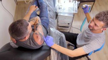 Tattoo artist fills a tattoo on the shoulder of a person with a tattoo machine