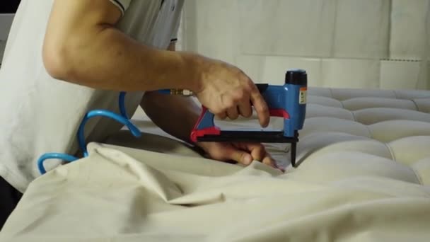 Man bekleding deel van het bed met een nieuwe stof met behulp van een meubelnietmachine — Stockvideo