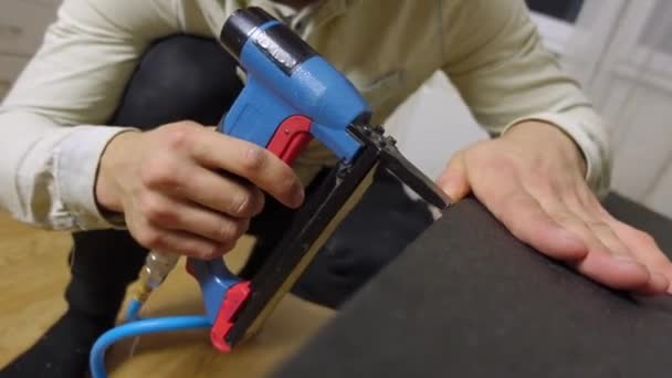 Man bekleding deel van het bed met een nieuwe stof met behulp van een meubelnietmachine — Stockvideo