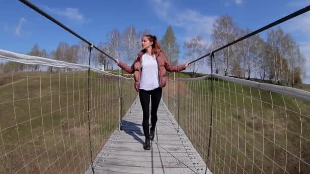 Frau läuft im Frühling auf einer Hängebrücke über einen kleinen Fluss in einem Nationalpark — Stockvideo