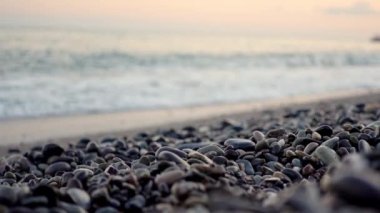 Çakıl taşı plajı ve pembe gün batımında bulanık deniz dalgaları. 