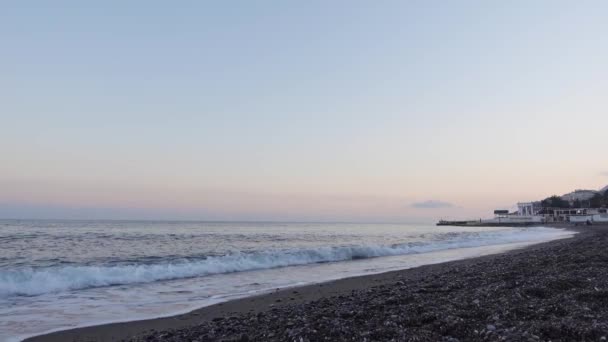Sandige Küste mit Kieselsteinen und blauen Meereswellen bei Sonnenuntergang — Stockvideo