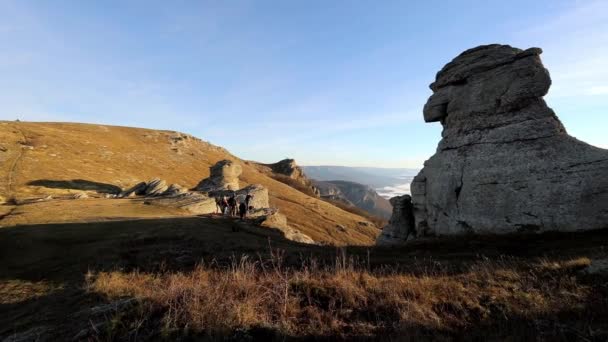 Люди на вершине горы стоят рядом с большой скалой, снимая пейзаж — стоковое видео