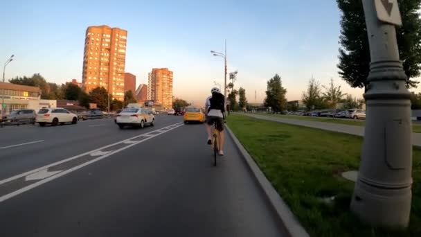 Cyklista jezdí na kole po rušné ulici mezi auty v létě. Zadní pohled — Stock video