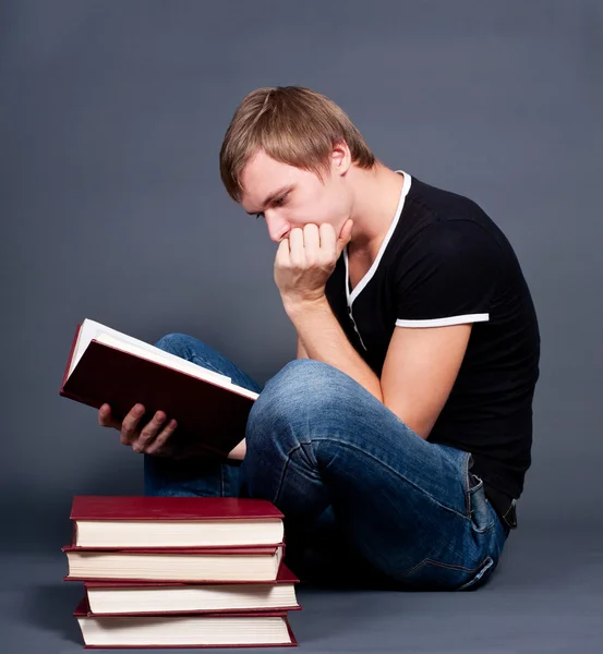 Töprengő fiatal ember tanul a verem a könyvek — Stock Fotó