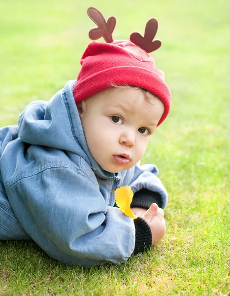 Boy in funny deer hat on grass with autumn leave — Stock Photo, Image