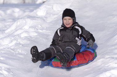 Happy boy slide down the hill. Cold winter.