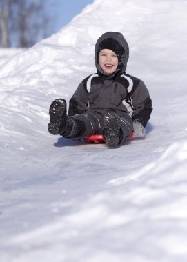 Happy boy slide down the hill. Cold winter.