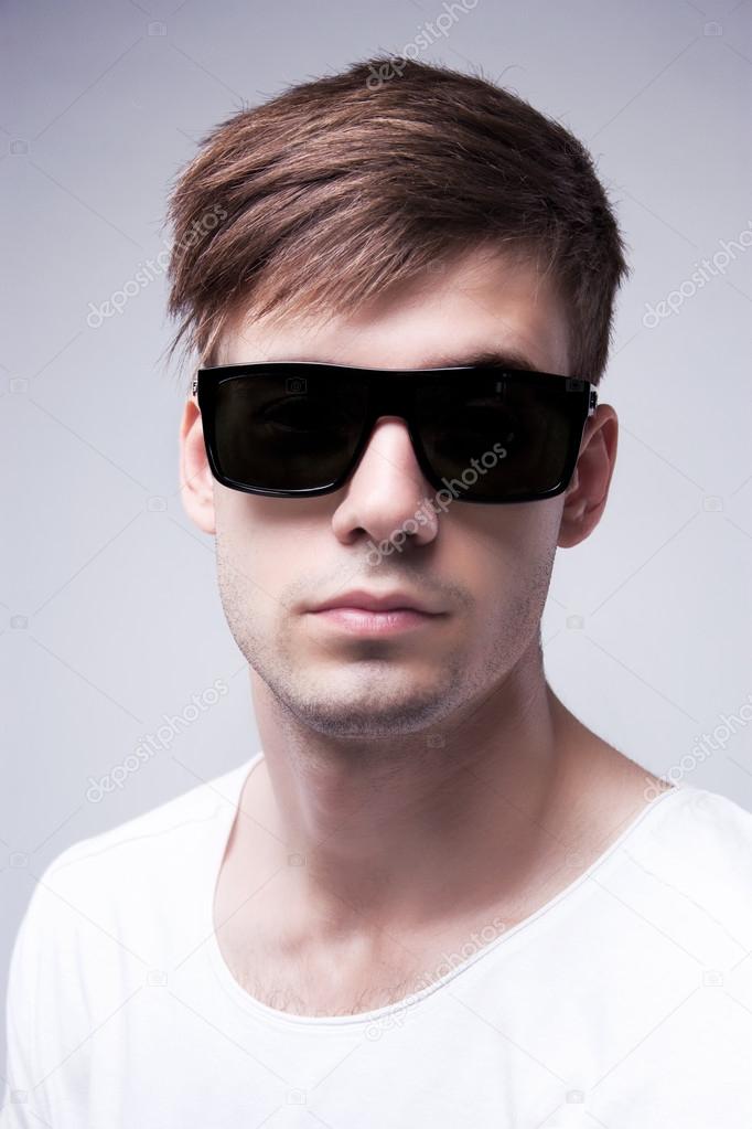 Close-up portrait of a young stylish beautiful man with black glasses on a grey background