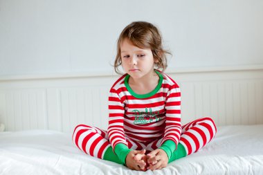 küçük kız yatağında oturup Çizgili Pijama içinde