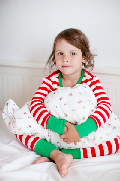 Liten flicka i randig pyjamas sitter på sin säng — Stockfoto