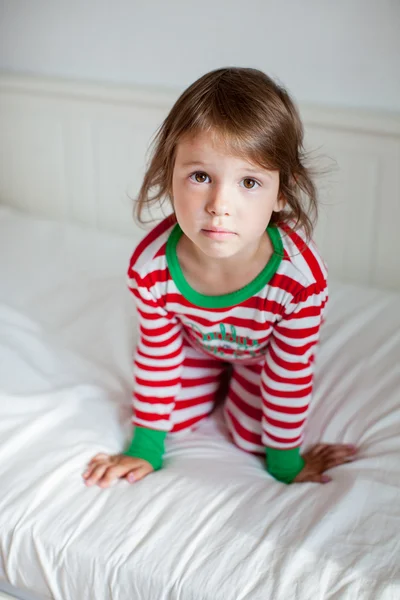 Porträtt av liten flicka i pyjamas som sitter på sängen — Stockfoto