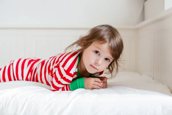 Liten flicka i randig pyjamas liggande på hennes säng — Stockfoto