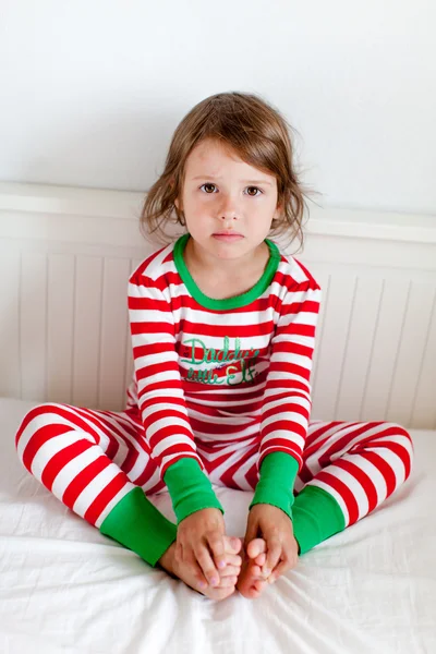 Petite fille en pyjama rayé assise sur son lit — Photo