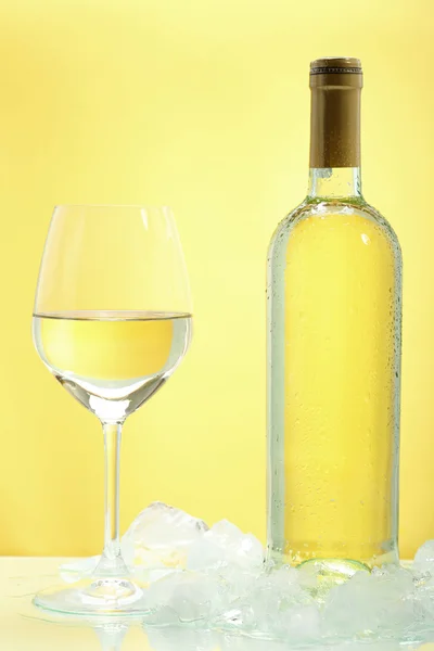 Bicchiere di vino bianco e bottiglia con ghiaccio su sfondo giallo — Foto Stock