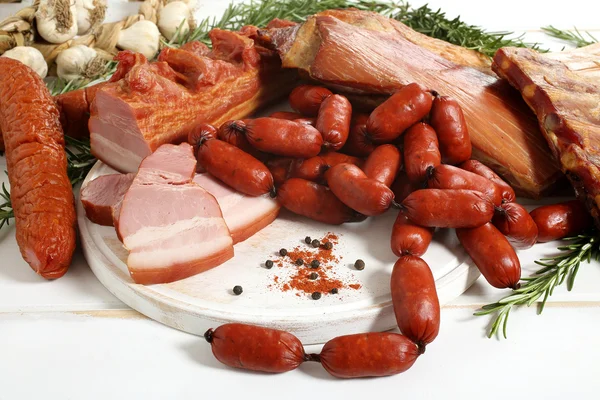 Вкусные копченые колбасы и бекон на белом деревянном столе — стоковое фото