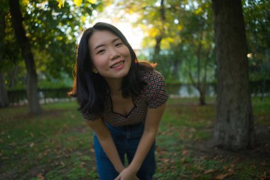 Mutlu ve güzel Asyalı Koreli kadın portresi şehir parkında gün batımında neşeli ve rahat bir şekilde özgür doğa ve sonbahar renklerinin tadını çıkarıyor.