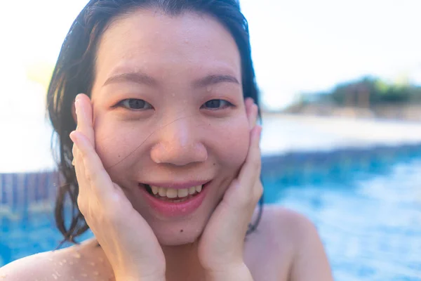 summer holidays natural portrait of young happy and attractive Asian Japanese woman enjoying relaxed and cheerful swimming pool at hotel resort in tourism travel concept