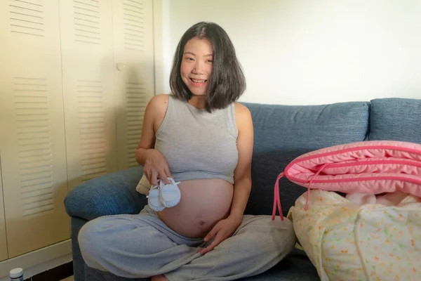 young happy and beautiful Asian Korean woman pregnant on couch enjoying playful and smiling relaxed at home in pregnancy and maternity concept