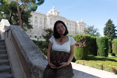 Genç, mutlu ve güzel Asyalı kadın dışarıda poz veriyor mutlu ve neşeli hamile karnını gösteriyor hamilelik ve hamilelik konseptinde gülümseyerek.