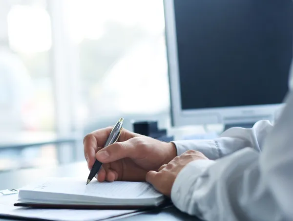 Empresario escribe en un cuaderno mientras está sentado en un escritorio — Foto de Stock