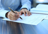 Geschäftsfrau sitzt am Schreibtisch und unterschreibt einen Vertrag mit seichtem Fokus auf Unterschrift