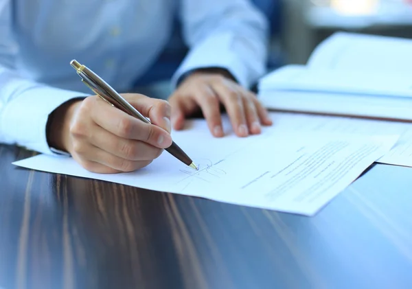 Empresária sentada na mesa do escritório assinando um contrato com foco superficial na assinatura — Fotografia de Stock