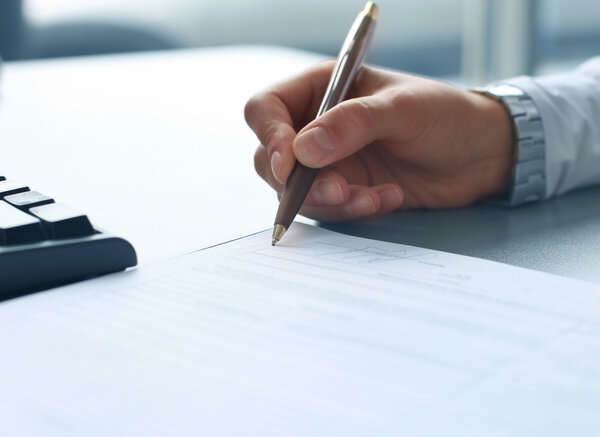 Businesswoman sitting at office desk signing a contract with shallow focus on signature.