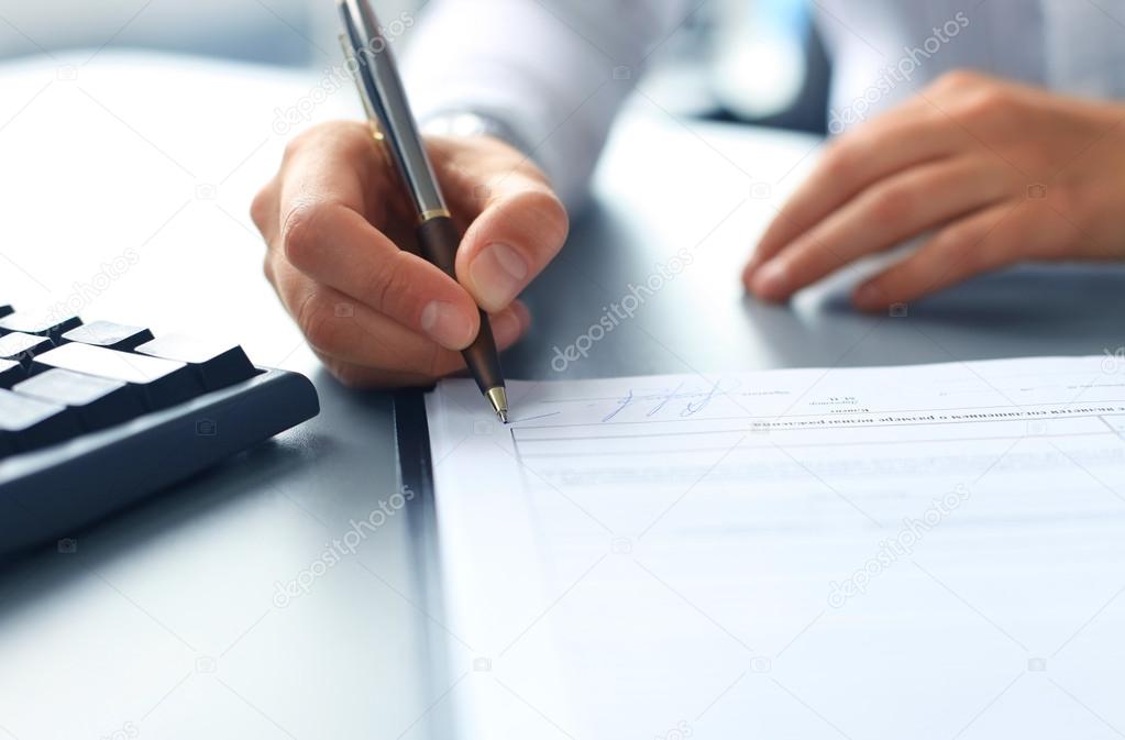 Businesswoman sitting at office desk signing a contract with shallow focus on signature