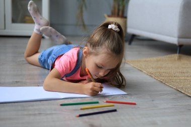 Gülümseyen mutlu kız, yanında oyuncak bir fille yerde uzanıyor. Yaratıcı aktivitelerden zevk alıyor. Albümlere resim çiziyor.