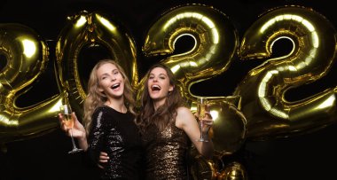 Şampanya içen iki genç bayan. Siyah arka planda izole edilmiş balonlu kızlar Noel 'de ya da 2022 yılbaşı partisinde eğleniyorlar.