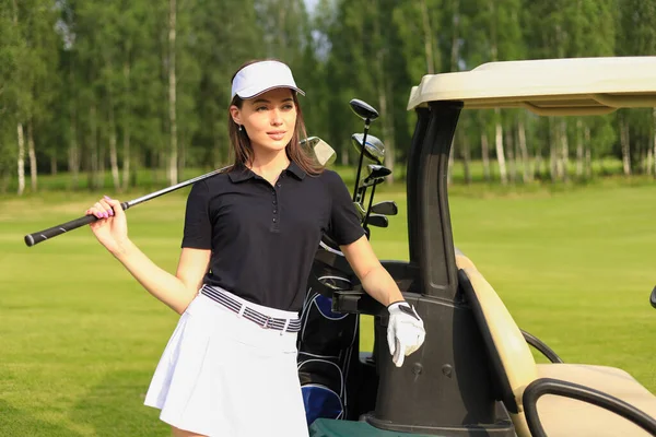 Güzel, neşeli kadın golf arabasının yanında duruyor.