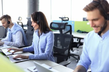 Office, arka planda çalışan meslektaşları ile kulaklık giyen kadın müşteri hizmetleri temsilcisi gülümseyen portresi