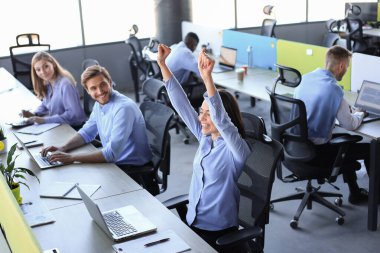 İnternette başarıyı kutlayan dizüstü bilgisayara bakan heyecanlı iş kadını ofiste oturuyor. E-postada iyi haber okuyan kadın.