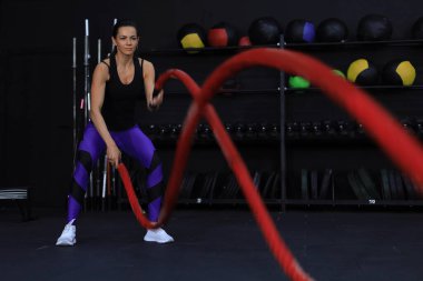 Formda bir kadın spor salonunda antrenman yaparken halat kullanıyor.