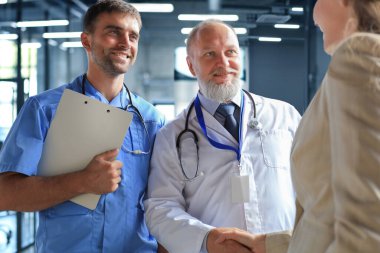 Modern bir tıp merkezindeki muayeneden önce iki doktor ve kadın hasta el sıkışıyor.