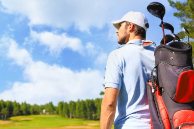 Golf oyuncusu yaz golfü sırasında yolda yürüyor ve çanta taşıyor.