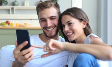 Mutlu çift, evdeki koltukta oturmuş akıllı bir telefonla medyadan zevk alıyor.