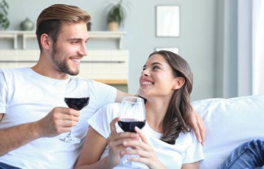 Genç bir çift oturma odasında bir bardak kırmızı şarap içiyor.