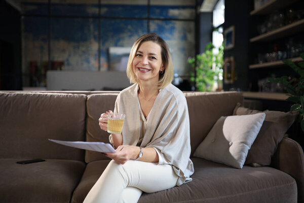 Middle aged woman smilling and happy about her finances. Attractive lady receiving good news from a paper mail.