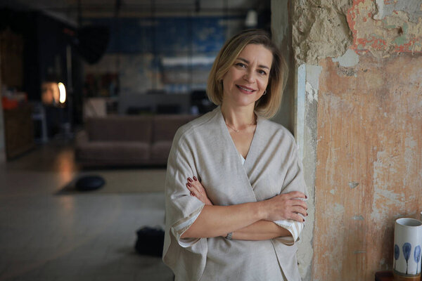 Confident stylish european middle aged woman standing at workplace, executive leader manager looking at camera