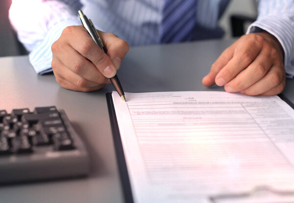Businessman sitting at office desk signing a contract with shallow focus on signature