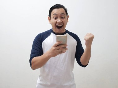 Mutlu, heyecanlı Asyalı genç adam bağırarak gülümsüyor ve akıllı telefonuna bakıp iyi haber konseptini alırken kazanan bir jest gösteriyor.