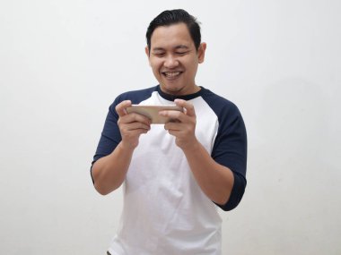 Komik suratlı mutlu Asyalı genç adam tablet akıllı telefonda oyun oynuyor.