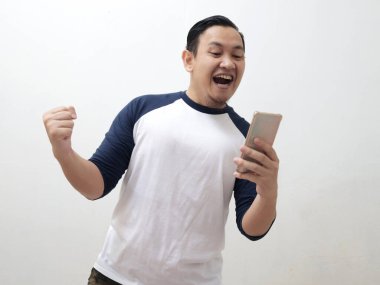 Mutlu, heyecanlı Asyalı genç adam bağırarak gülümsüyor ve akıllı telefonuna bakıp iyi haber konseptini alırken kazanan bir jest gösteriyor.