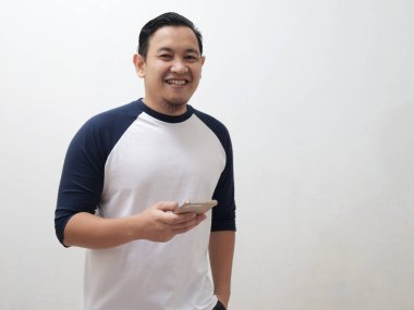 Telefonunu beyaz arka planda tutarken kameraya gülümseyen mutlu, genç Asyalı adam.