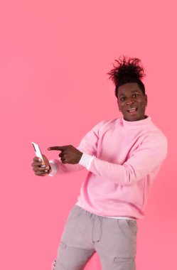 Exited afro american male pointing happy good news on his smartphone in pink clothes and background