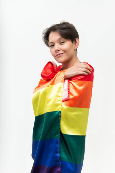 young gay woman dressed in the LGBT flag as a symbol of gender struggle looking at the camera in front of a white background