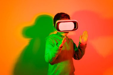 Latin boy playing with virtual reality glasses in front of colored lights background with his hands in front. High quality photo